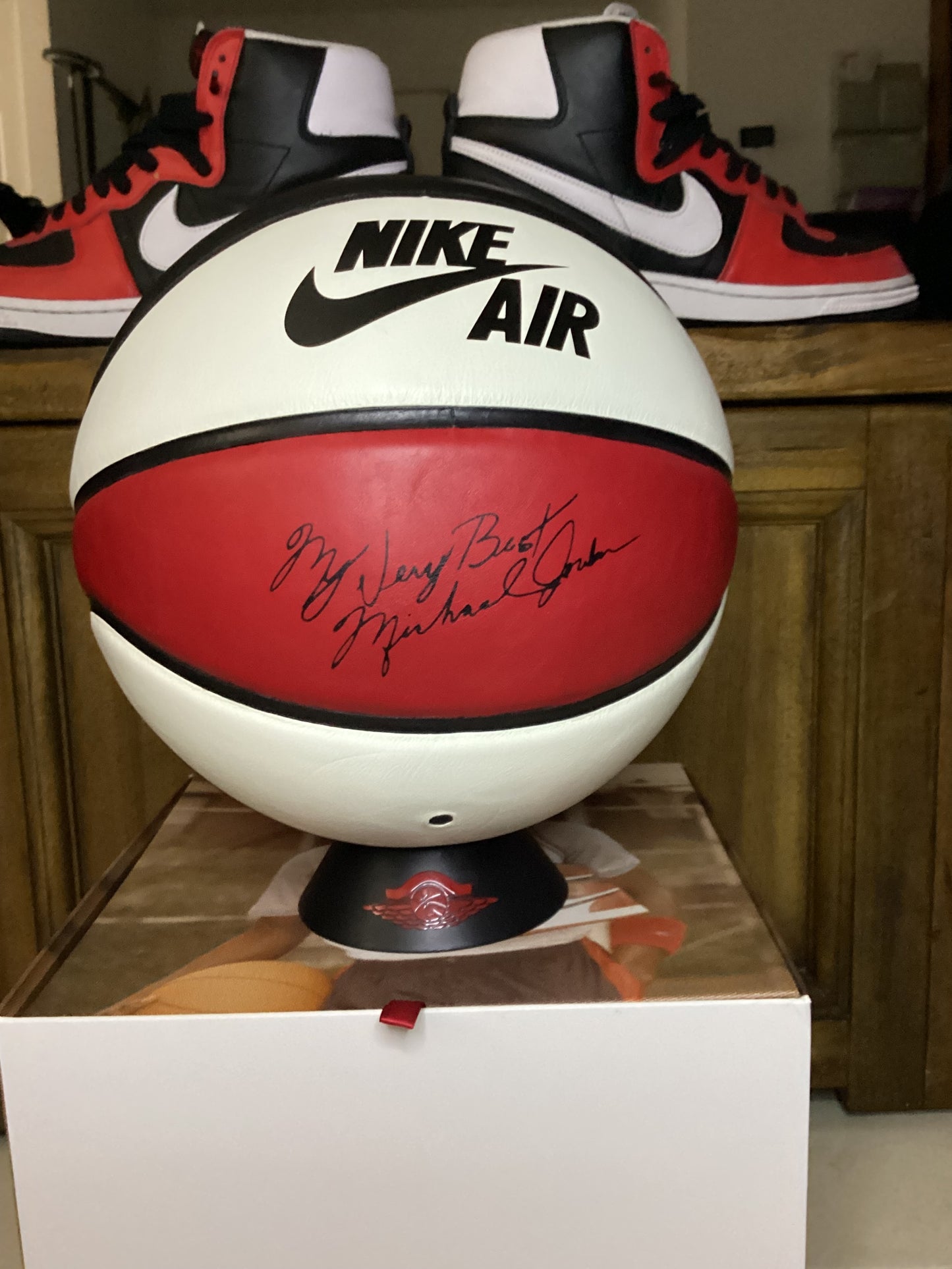 Nike x Jordan Heritage red, white, and black basketball with Nike Air branding and red signature-style writing, displayed on a wooden shelf with sneakers in the background