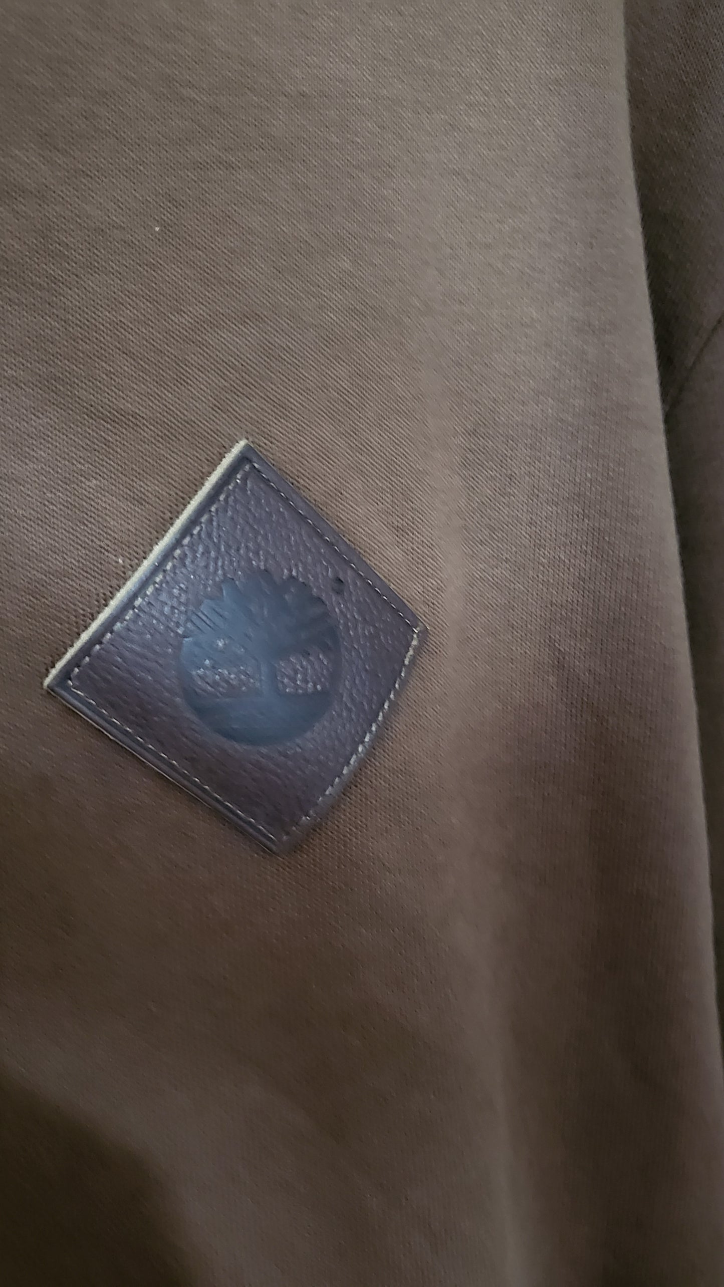 Close-up of Timberland leather chest patch logo on brown hoodie fabric