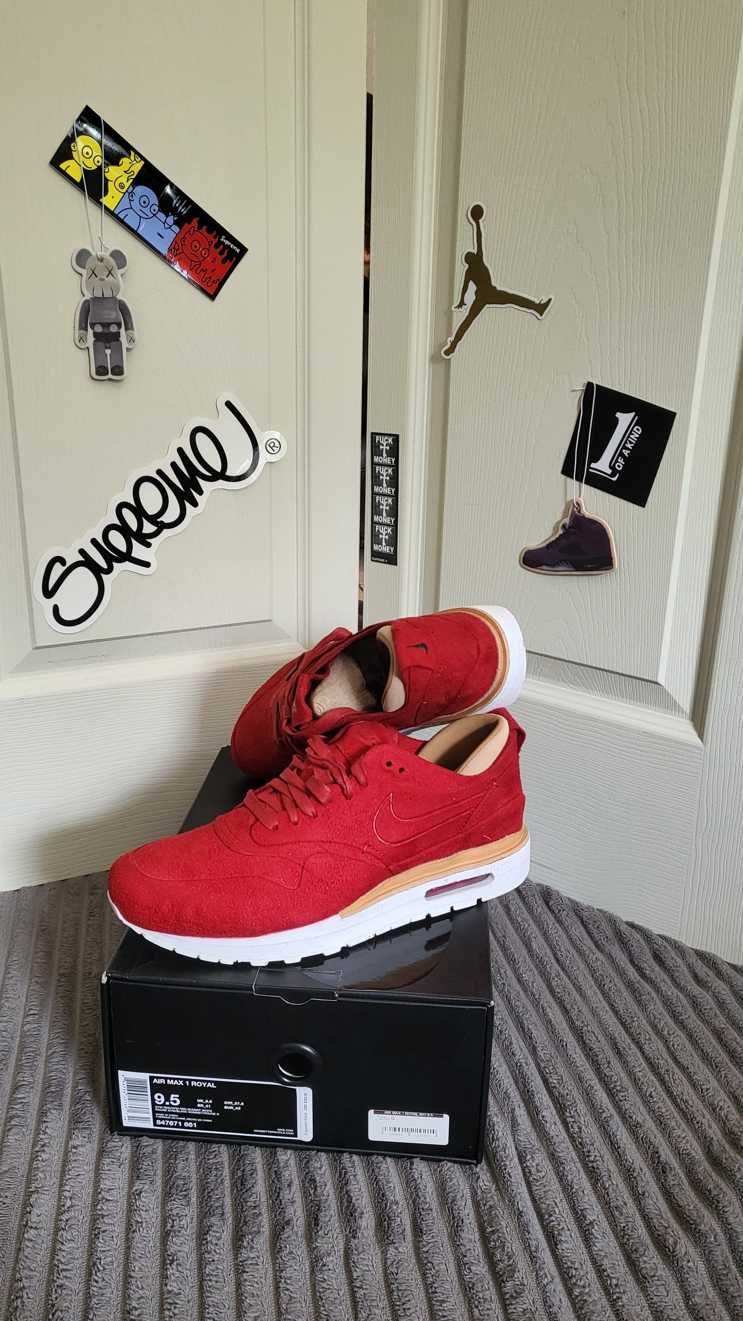 Frontal shot of Nike Air Max 1 Royal “Gym Red” with worn insoles and bold red uppers, placed in front of decorated door.