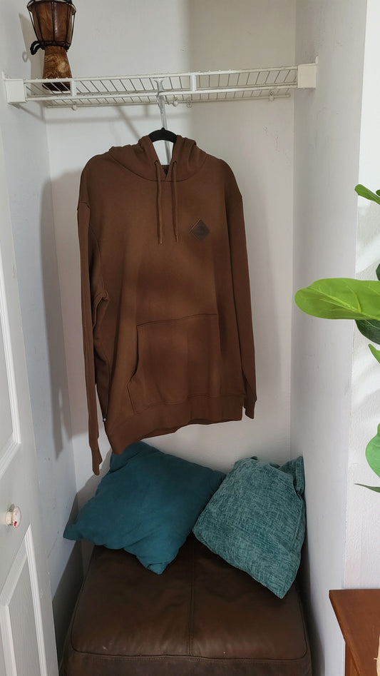 Front view of Timberland brown pullover hoodie with drawstrings, size L, hanging in corner room with pillows and plant